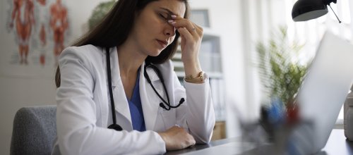 Frustrierte Ärztin sitzt am Schreibtisch vor ihrem Laptop.