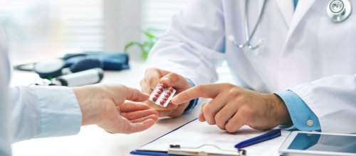 Man sieht auf dem Bild die Hände eines Arztes, der gerade Medikamente an einen Patienten übergiibt.