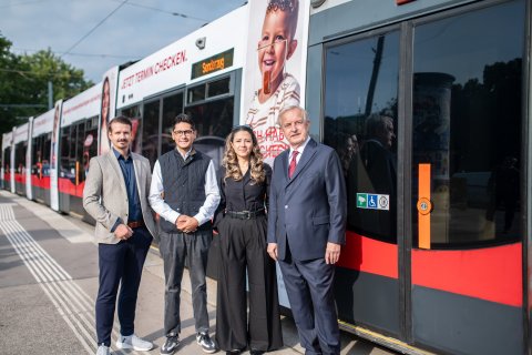 Drei Männer und eine Frau stehen neben einer Straßenbahn