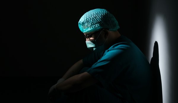 Mann in OP-Kleidung sitzt nachdenklich im Dunkeln
