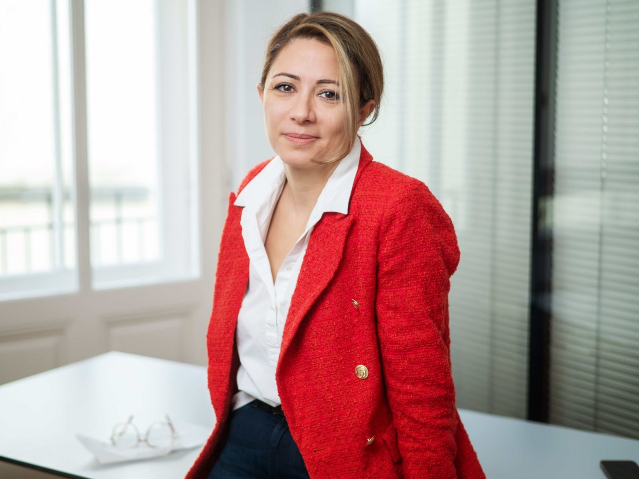 Naghme Kamaleyan-Schmied, Kurienobfrau der niedergelassenen Ärzte in der Kammer für Ärztinnen und Ärzte in Wien bei einem Tisch stehend und blickt in die Kamera - in einem Büro mit Fenster und gläsernen Trennwänden.