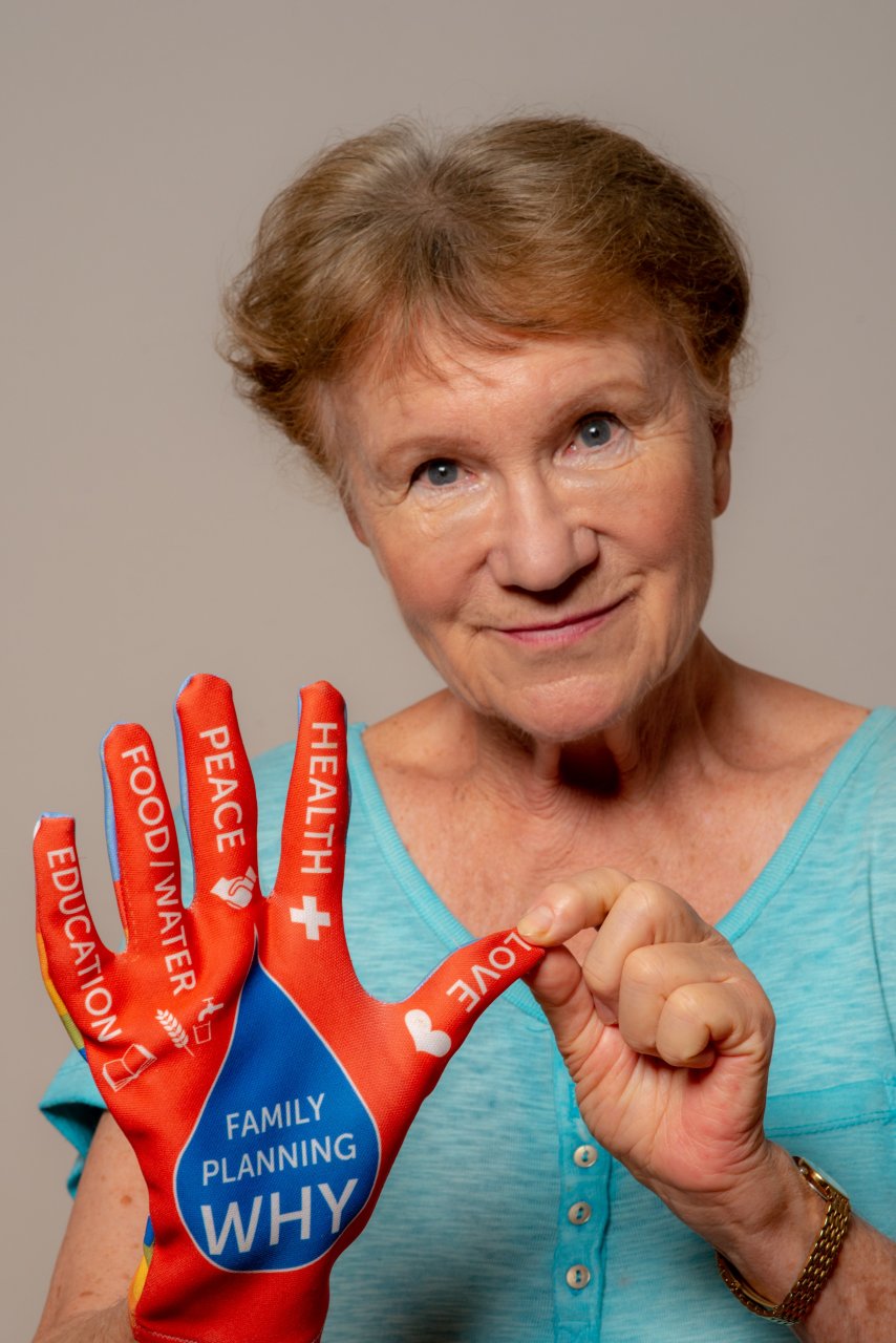 Frau Maria Hengstberger hat einen Handschuh an, auf dem verschiedene Wörter auf Englisch stehen: Love, Health, Peace, Food/Water und Education.