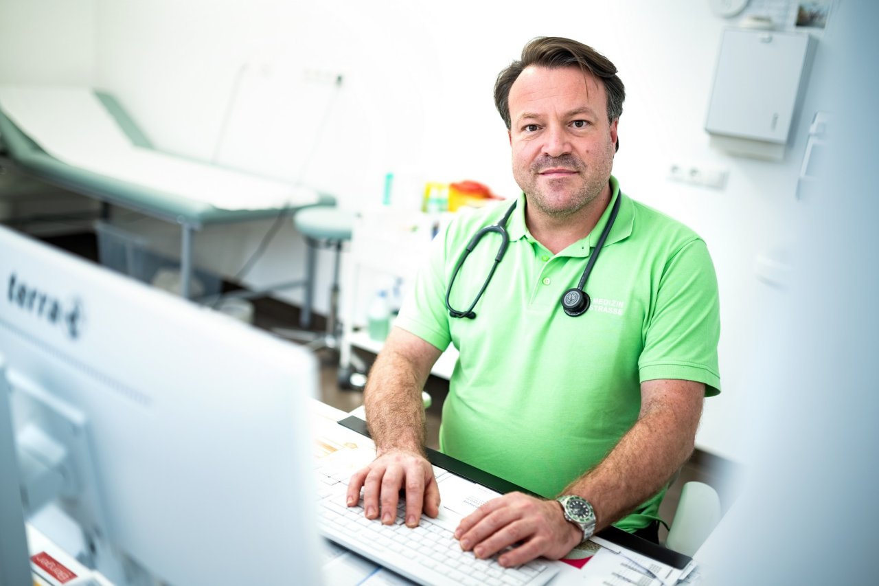 Arzt mit Stethoskop, am Schreibtisch in der Ordination