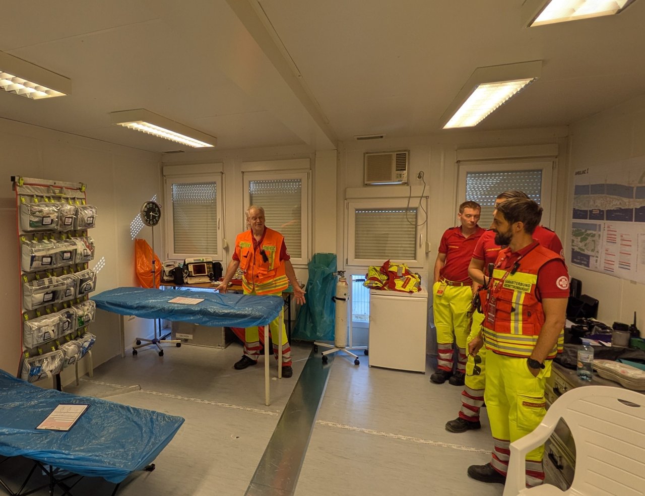 Man sieht vier Männer auf dem Foto, die in einem Raum stehen. Dieser ist wie eine provisorische Notfallstelle eingerichtet.