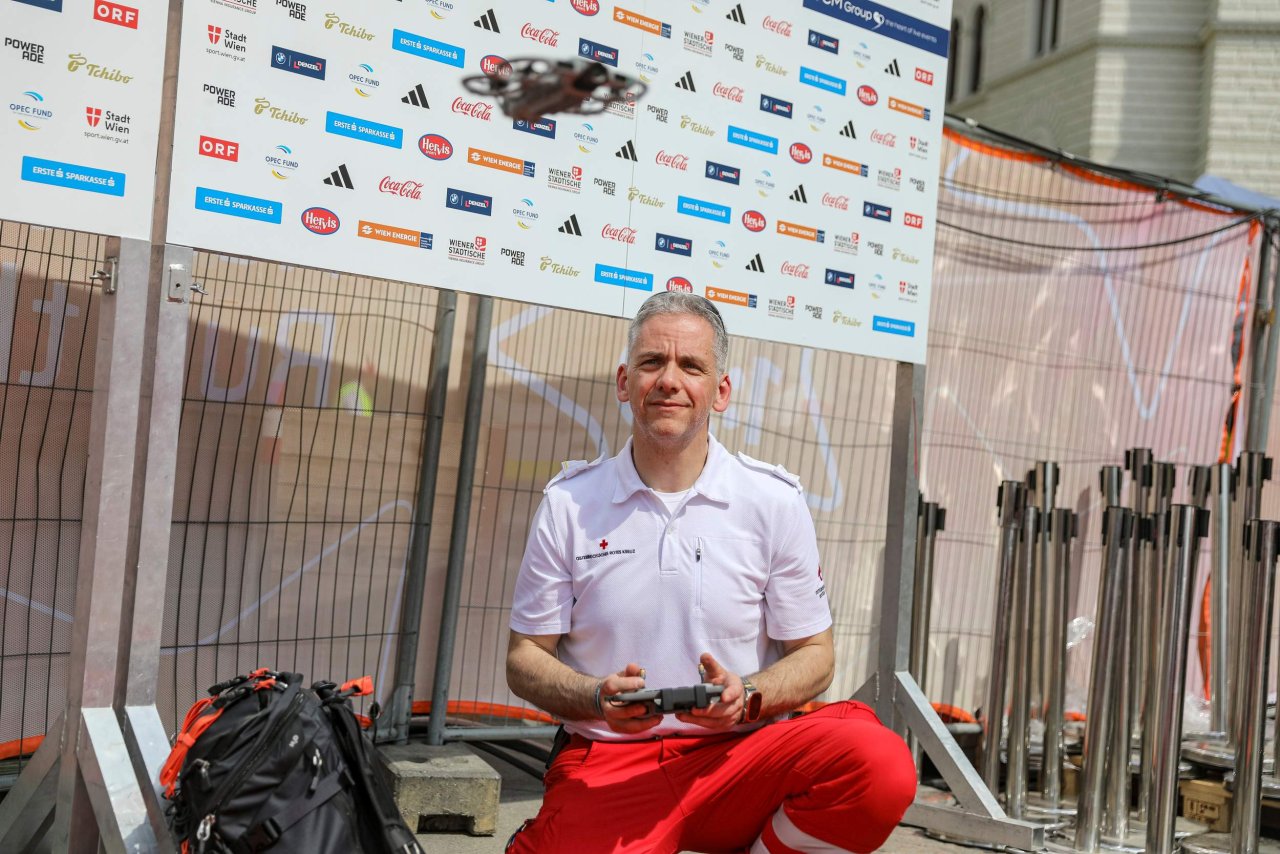 Ein Mann bedient mit einer Fernsteuerung eine vor bzw. leicht über ihm fliegende Drohne.