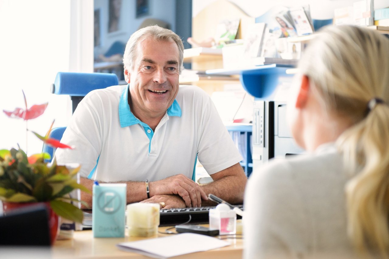 Arzt sitzt Patientin am Schreibtisch in der Ordination gegenüber.
