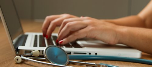 Laptop und Hände mit danebenliegendem Stethoskop