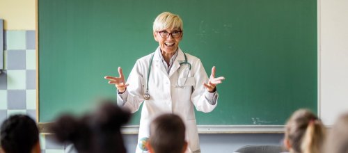 Eine Ärztin steht im Klassenzimmer und unterrichtet Gesundheit.