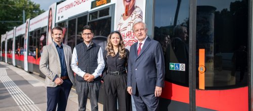 Drei Männer und eine Frau stehen neben einer Straßenbahn