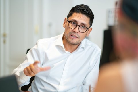 Eduardo Maldonaldo-González, Vizepräsident der Kammer für Ärztinnen und Ärzte in Wien, im Gespräch. Er sitzt an einem Tisch , spricht und gestikuliert mit seiner rechten Hand.