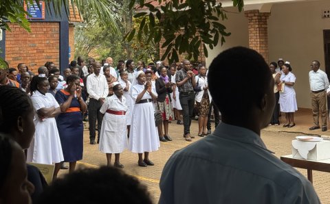 Eine Aufnahme in einem Hof in Uganda. Es stehen mehrere Personen im Hof eines Spitals zur Morgenbesprechung. 