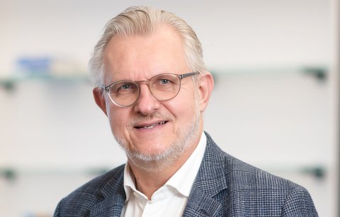 Mann mit Brille, Hemd und Sakko lächelt in die Kamera.