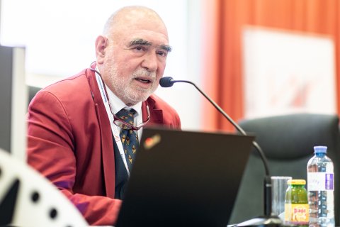 Mann in rotem Sakko, der in ein Mikrofon spricht 