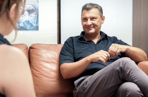 Mann mit kurzärmligem Hemd sitzt im Gespräch auf einem Sofa. 