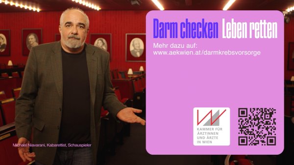 Der Kabarettist Michael Niavarani steht in einem mit roten Wänden und Bildern versehenen Raum.