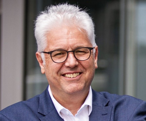 Mann mit Brille, Hemd und Sakko lächelt in die Kamera.