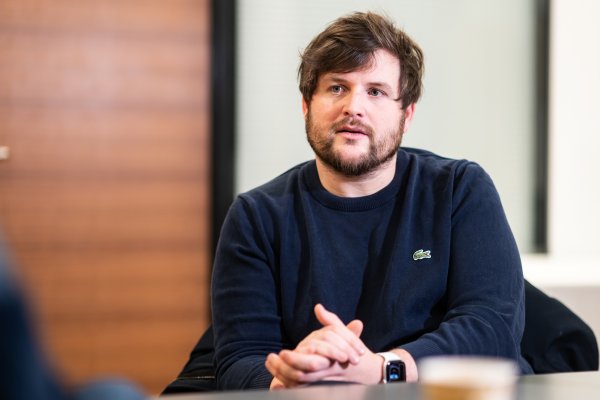 Porträtbild von jungem Mann mit verschränkten Händen und blauem Pullover in Gesprächssituation 